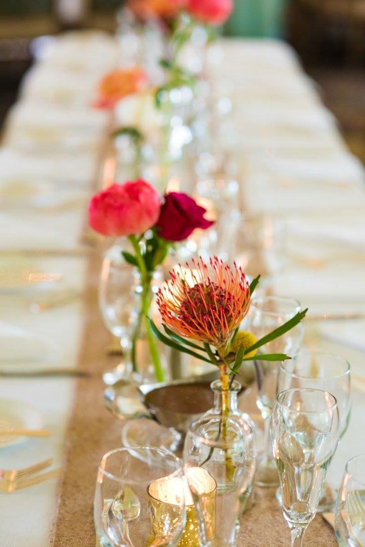 the table is set with many glasses and vases filled with flowers on each side