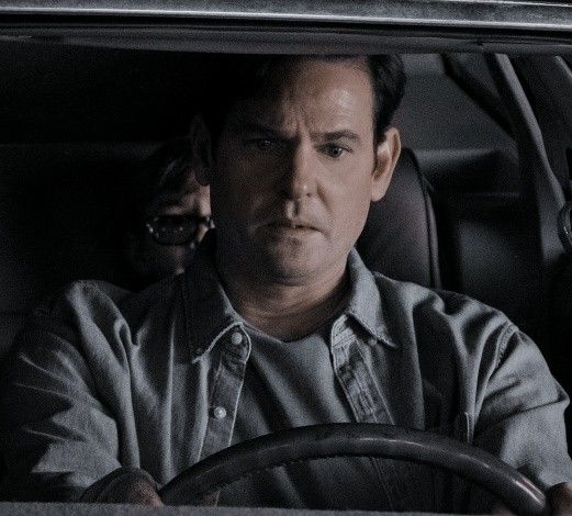 a man sitting in the driver's seat of a car with his hands on the steering wheel