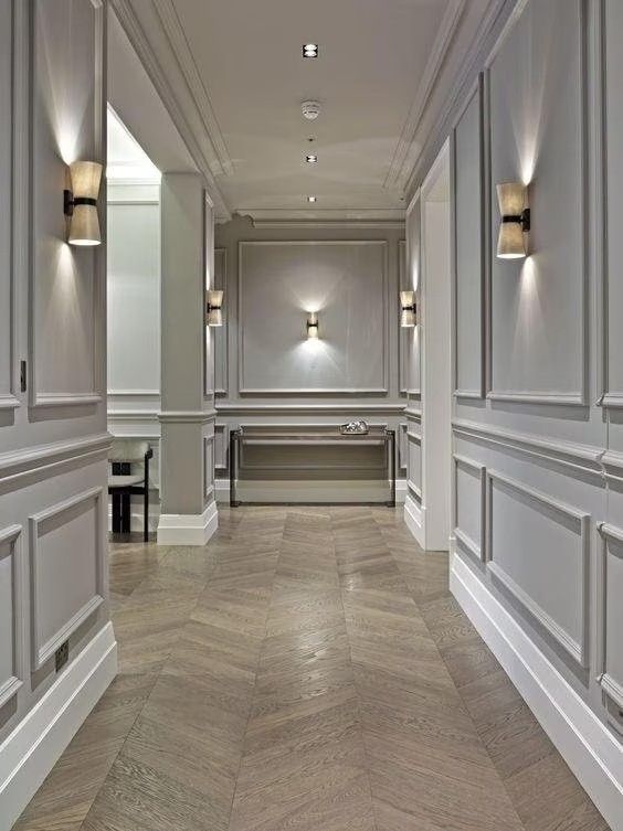 a long hallway with white walls and wood floors, along with two lamps on the wall