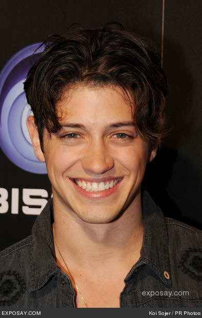 a smiling young man with dark hair and black shirt is posing for the camera at an event