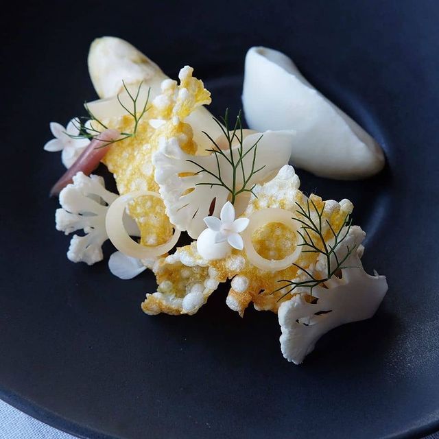 some kind of food on a black plate with white and yellow flowers in the middle