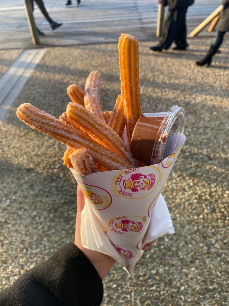 a person holding up a cup filled with churros