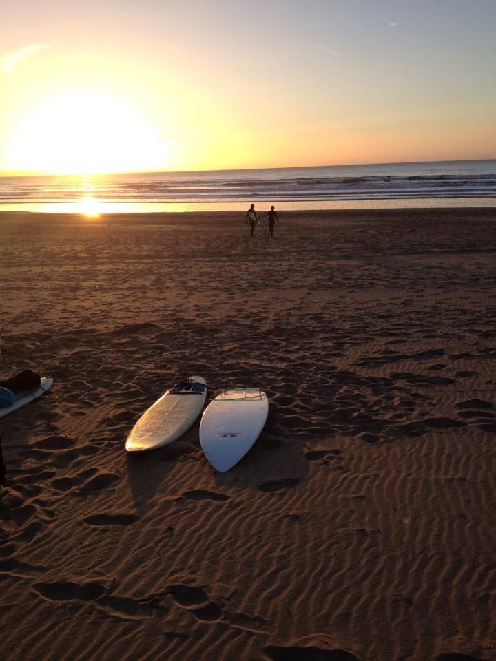 two surfboards are laying on the beach as the sun sets over the ocean in the background