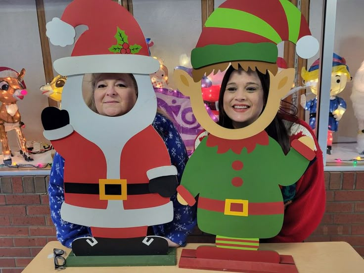 two women standing next to each other in front of some christmas decorations and santa hats