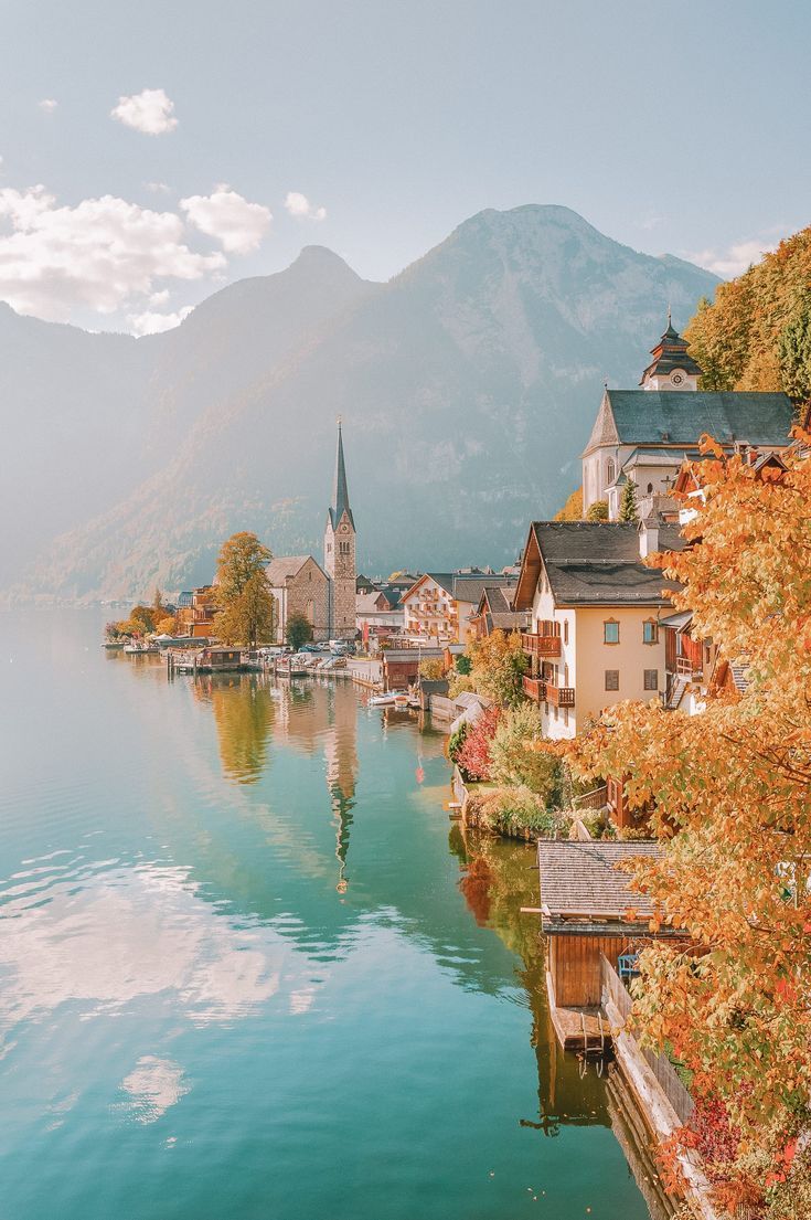 a lake surrounded by mountains with houses on the shore and trees in front of it