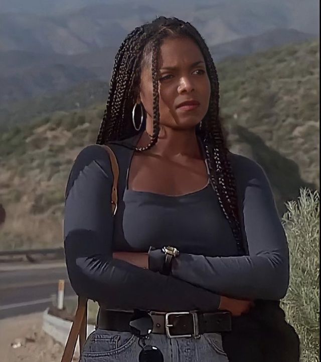 a woman with braids standing on the side of a road in front of mountains