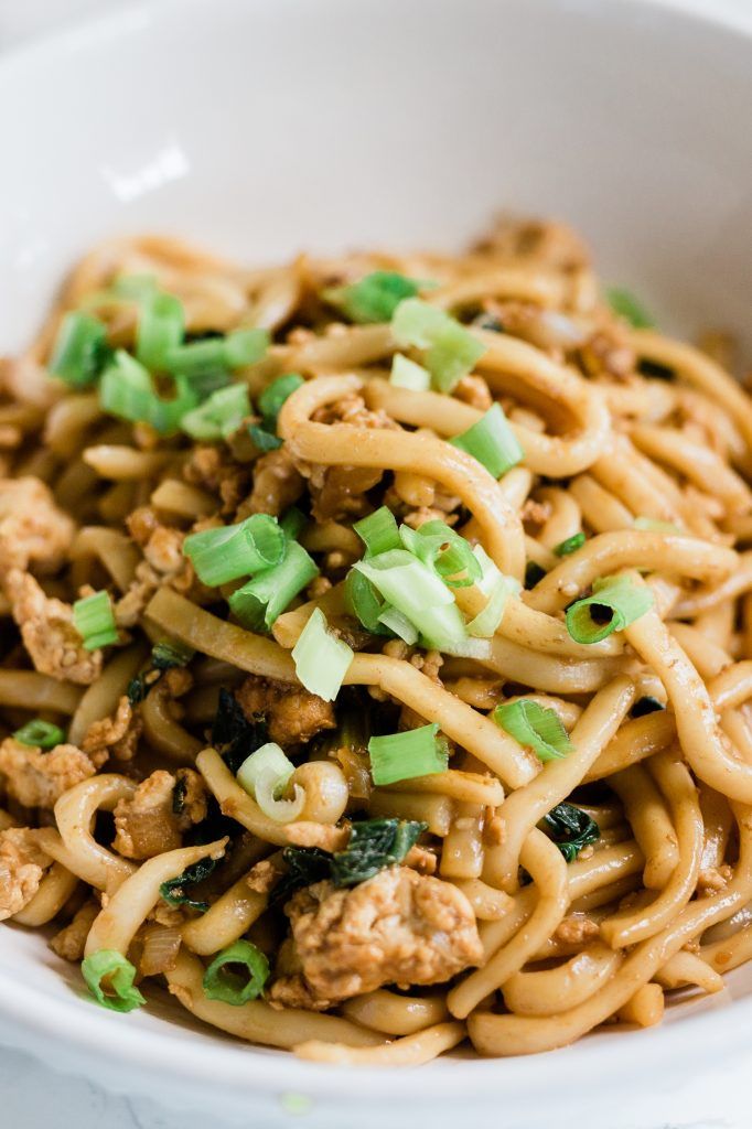 a white bowl filled with noodles and meat covered in green onions on top of a table