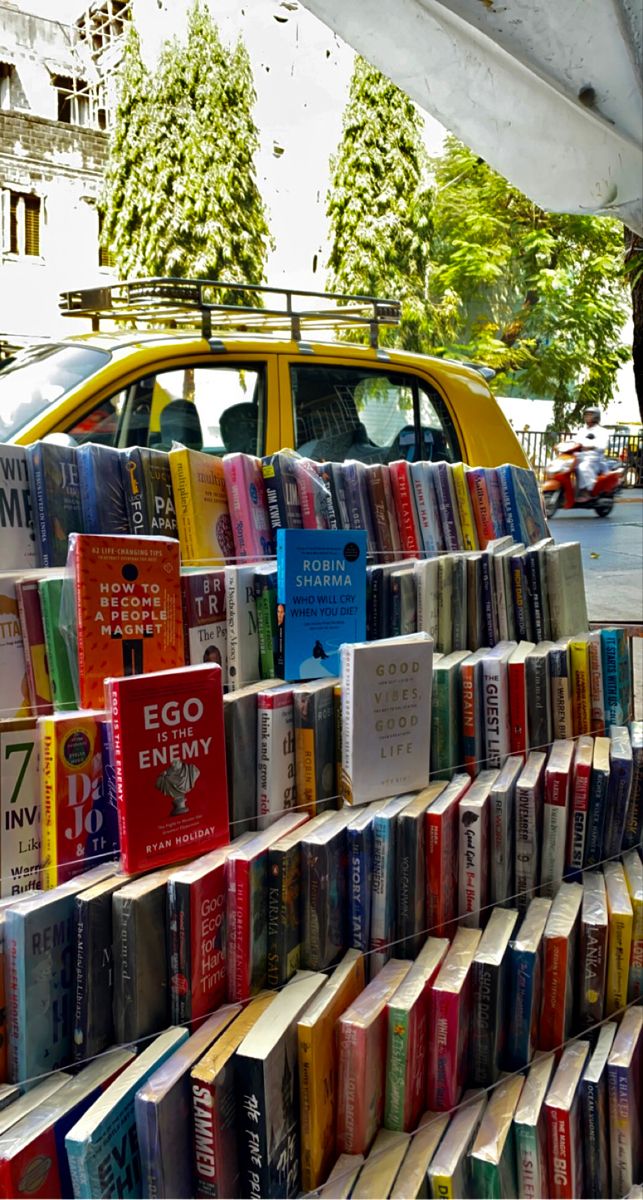 many books are stacked on top of each other in front of a yellow car and tree