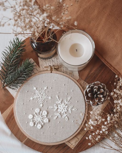 a cross stitch snowflake on a table next to a candle and some pine cones