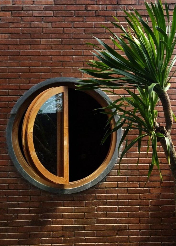 a round window on the side of a red brick wall next to a palm tree