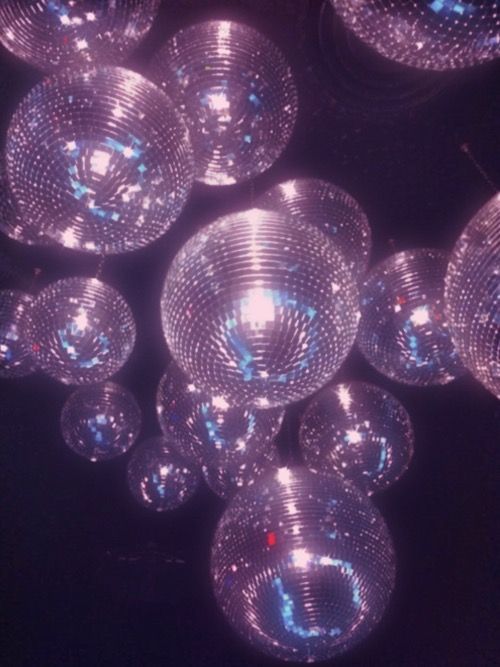 many shiny disco balls are hanging from the ceiling in front of a black background with blue lights