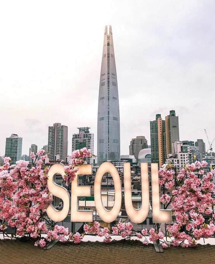 the word seoul spelled out with flowers in front of a cityscape and skyscrapers