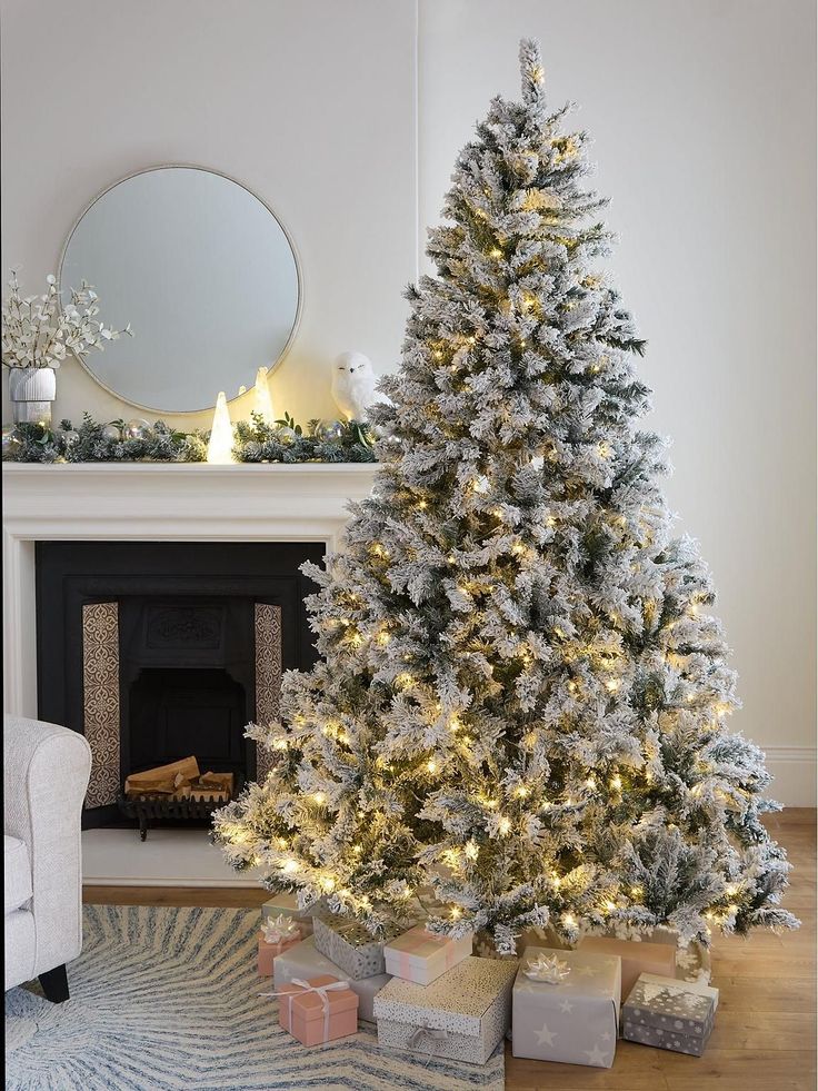 a white christmas tree in front of a fireplace with presents under it and a mirror on the wall