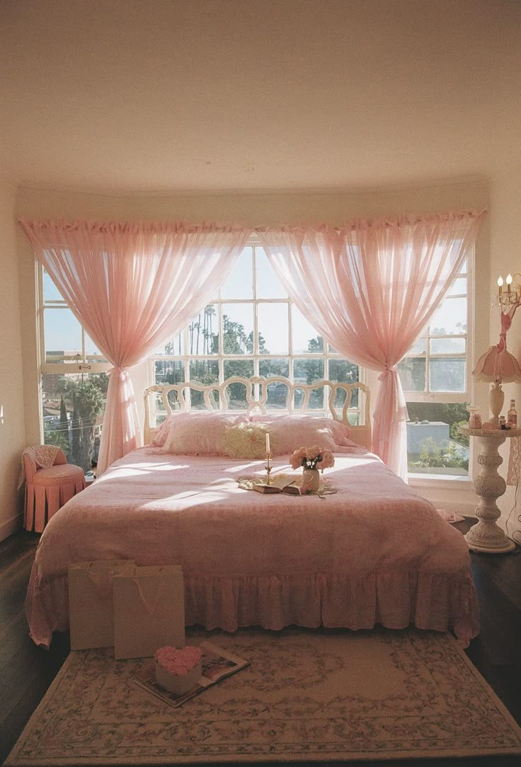 a bedroom with pink bedding and curtains in front of a large window that looks out onto the water