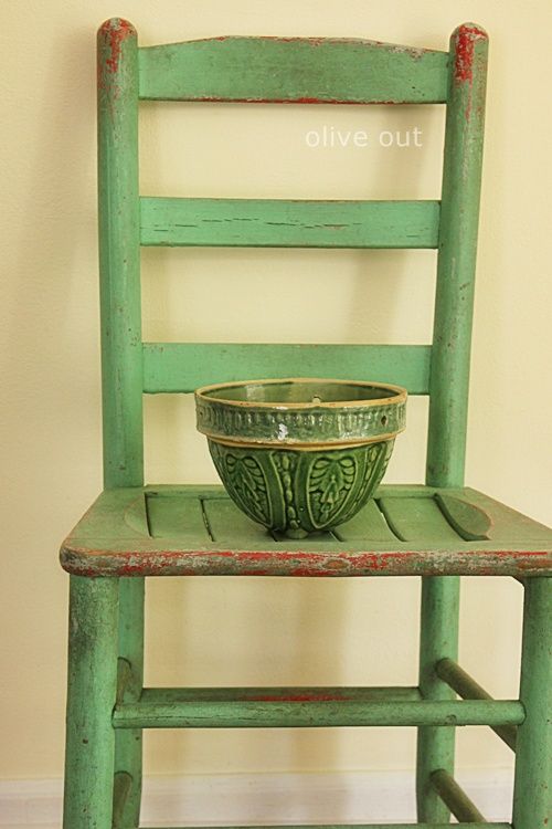 a green wooden chair with a bowl on it's back and legs, against a beige wall