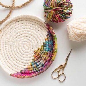 yarn and scissors on a white surface next to a basket with multicolored beads