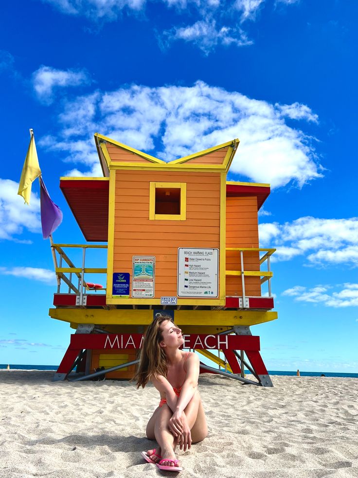 a woman is sitting on the beach in front of a lifeguard's tower