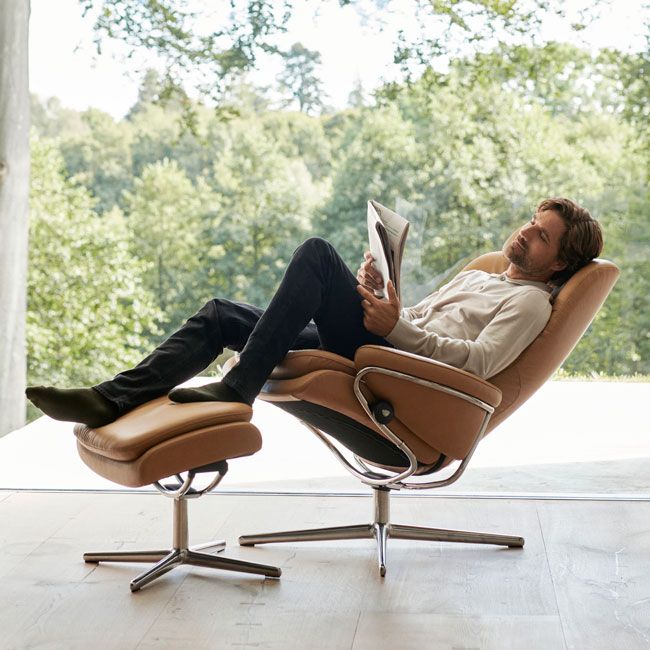 a man sitting in a chair and reading a book with his feet up on an ottoman