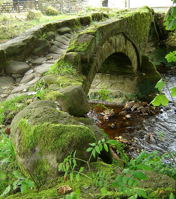 a stone bridge with moss growing on it's sides and water running under it