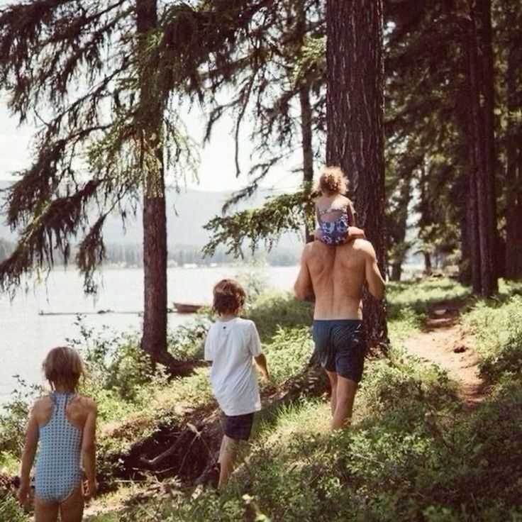 three people are walking in the woods near water