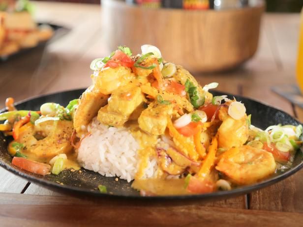 a black plate topped with chicken and veggies on top of a wooden table