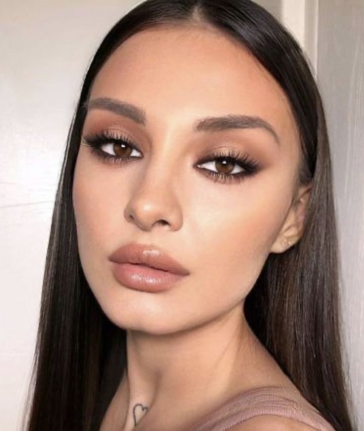 a woman with long hair and brown eyeshadow is posing for a photo in front of a white wall