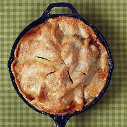 an apple pie in a cast iron skillet on a green checkered tablecloth