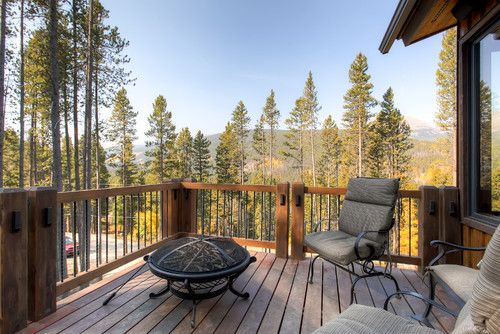 a wooden deck with two chairs and a fire pit on top of it, surrounded by pine trees