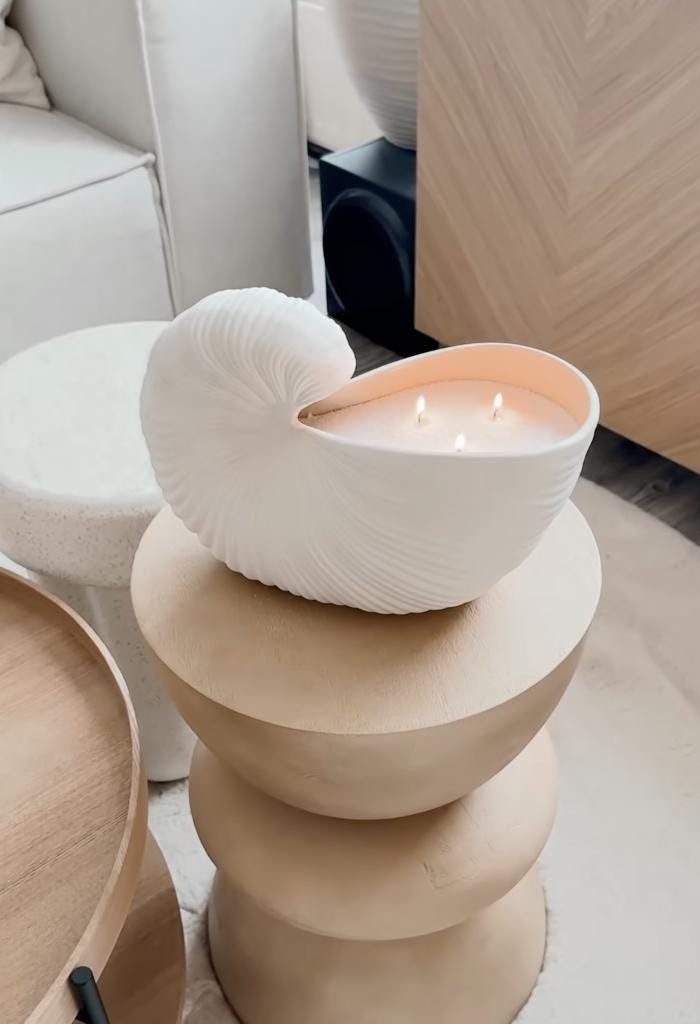 a white candle sitting on top of a stack of round wooden stools next to a couch