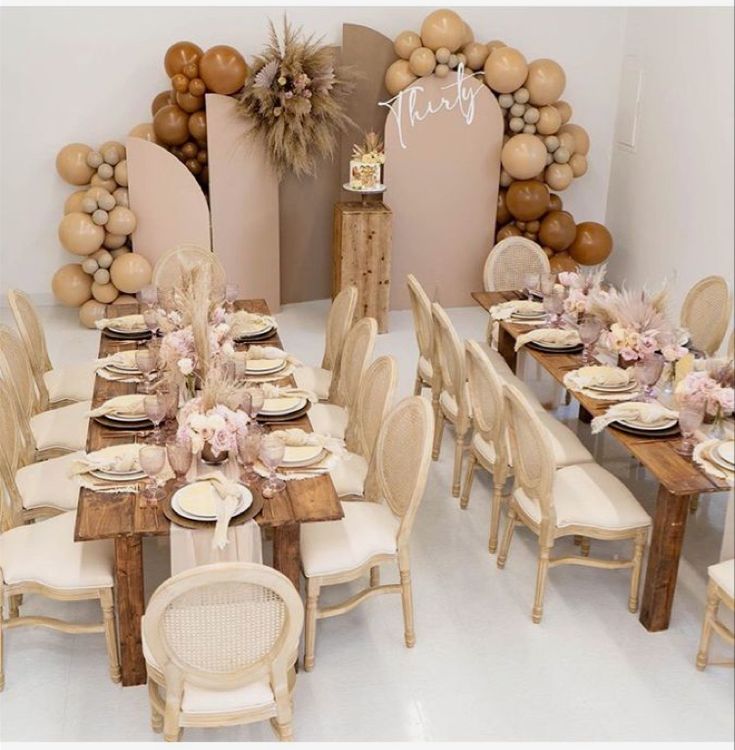 a table set up for a party with balloons in the shape of an arch and chairs