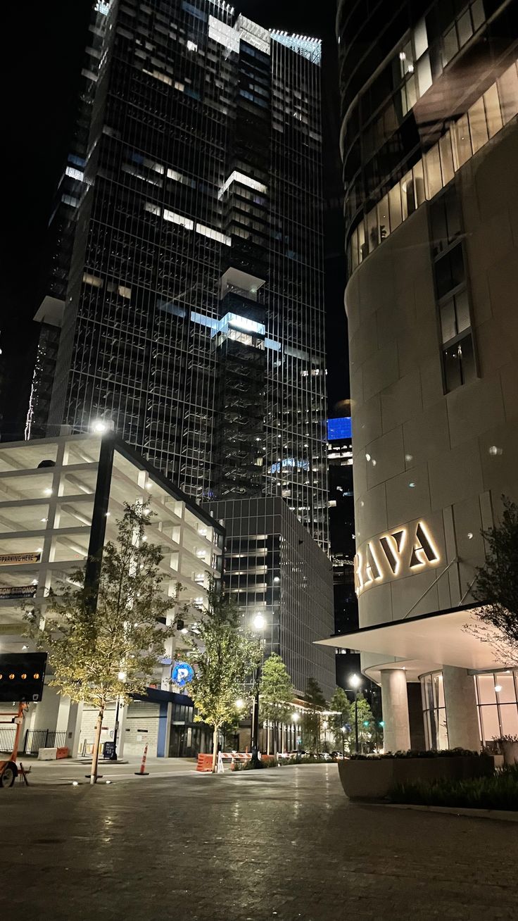 an empty city street at night with tall buildings in the background and lit up lights