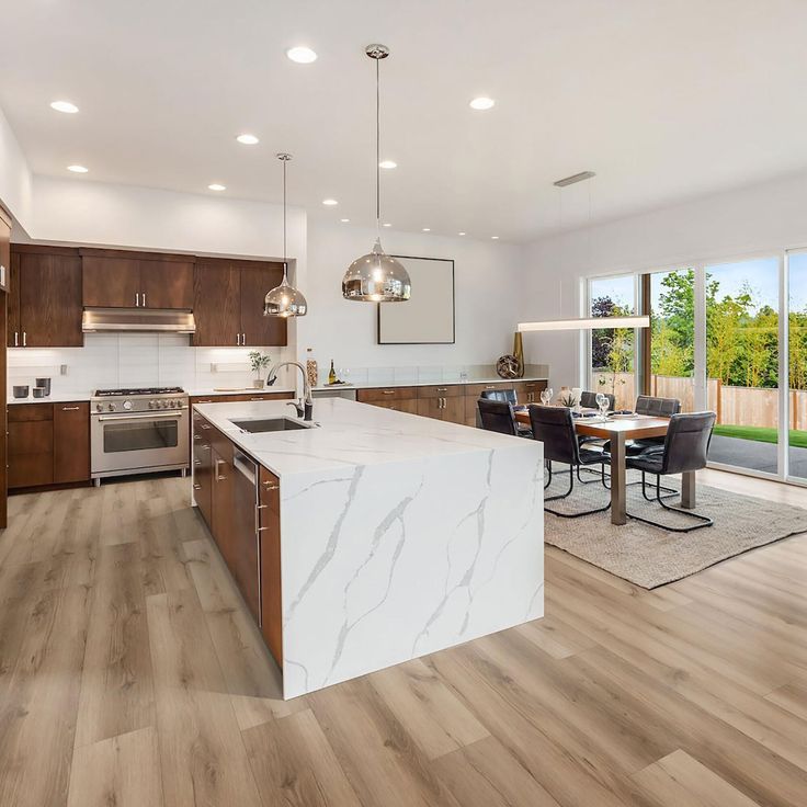 an open kitchen and dining room with wood flooring, marble counter tops and stainless steel appliances