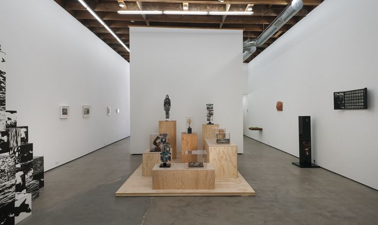 an art gallery with sculptures and photographs on the walls, in front of a white wall