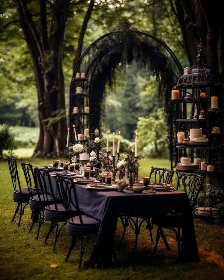 an outdoor dining table with candles and cake on it in the middle of a forest