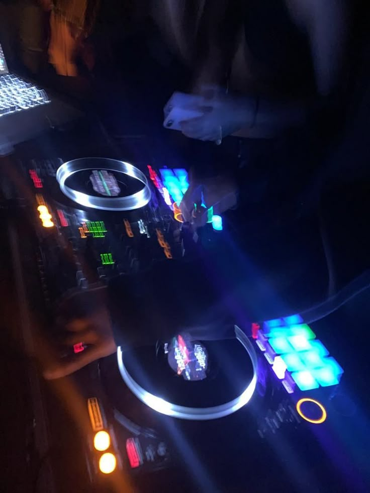 the dj is mixing music on his turntable in the dark with bright lights coming from behind him