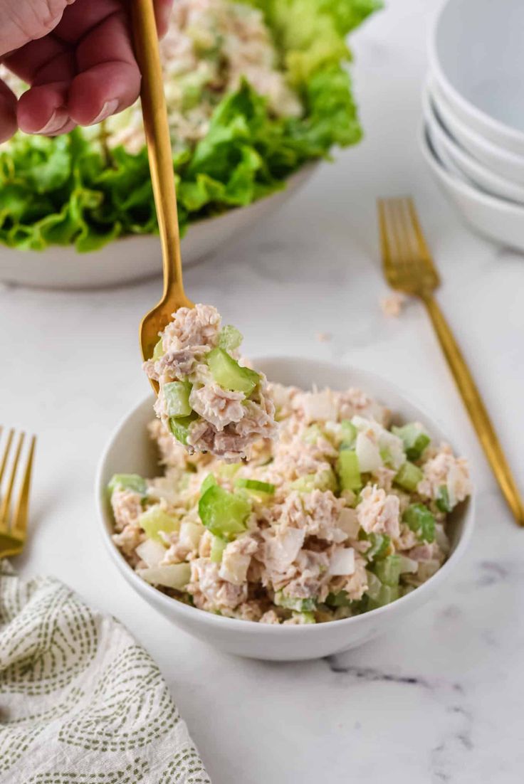 a person is holding a spoon over a bowl of tuna salad with lettuce