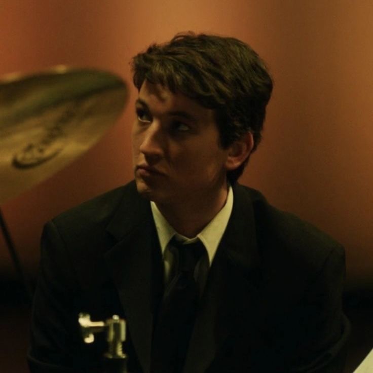 a man in a suit and tie sitting next to a drum set