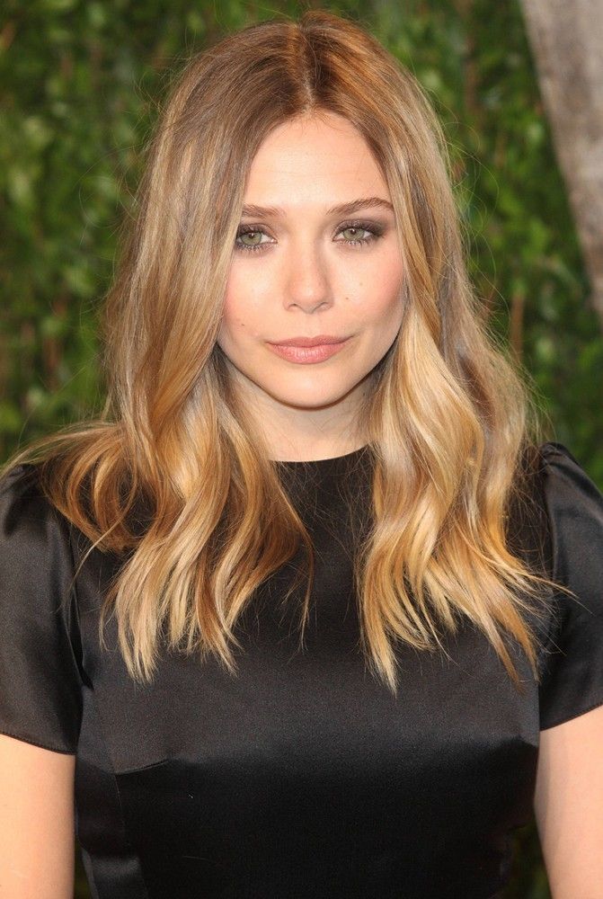 a woman with blonde hair and black dress posing for the camera in front of a green wall