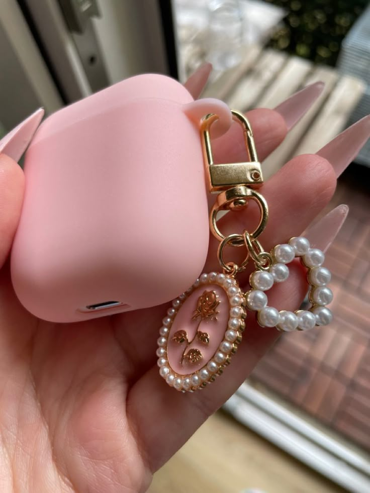 a hand holding a pink case with pearls on it and a keychain attached to it