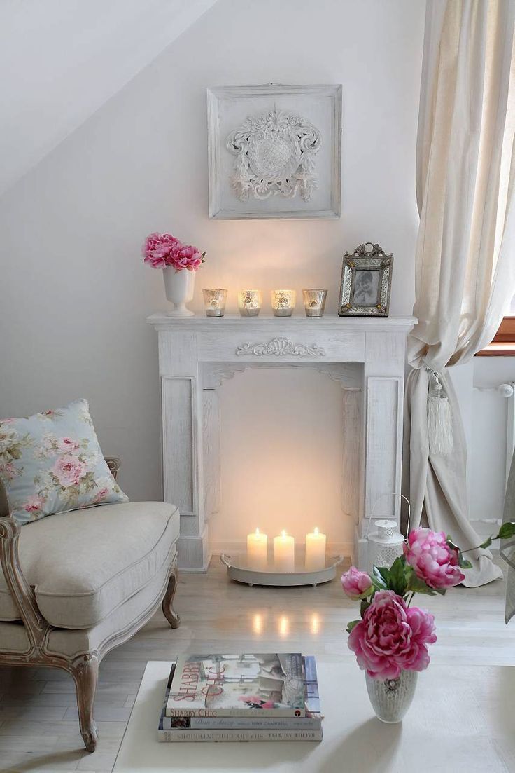 a living room filled with white furniture and pink flowers on the fireplace mantels