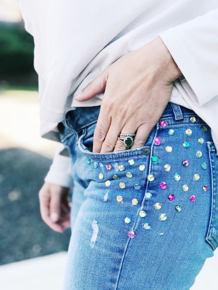 a woman with her hand in the pocket of her jean pants that has colorful studs on it