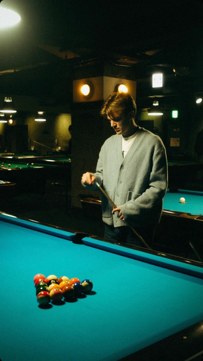 a man standing next to a pool table holding a cue in one hand and a ball in the other