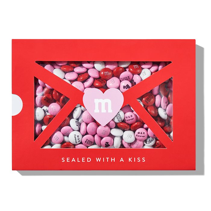 a red box filled with lots of pink and white candies next to a heart