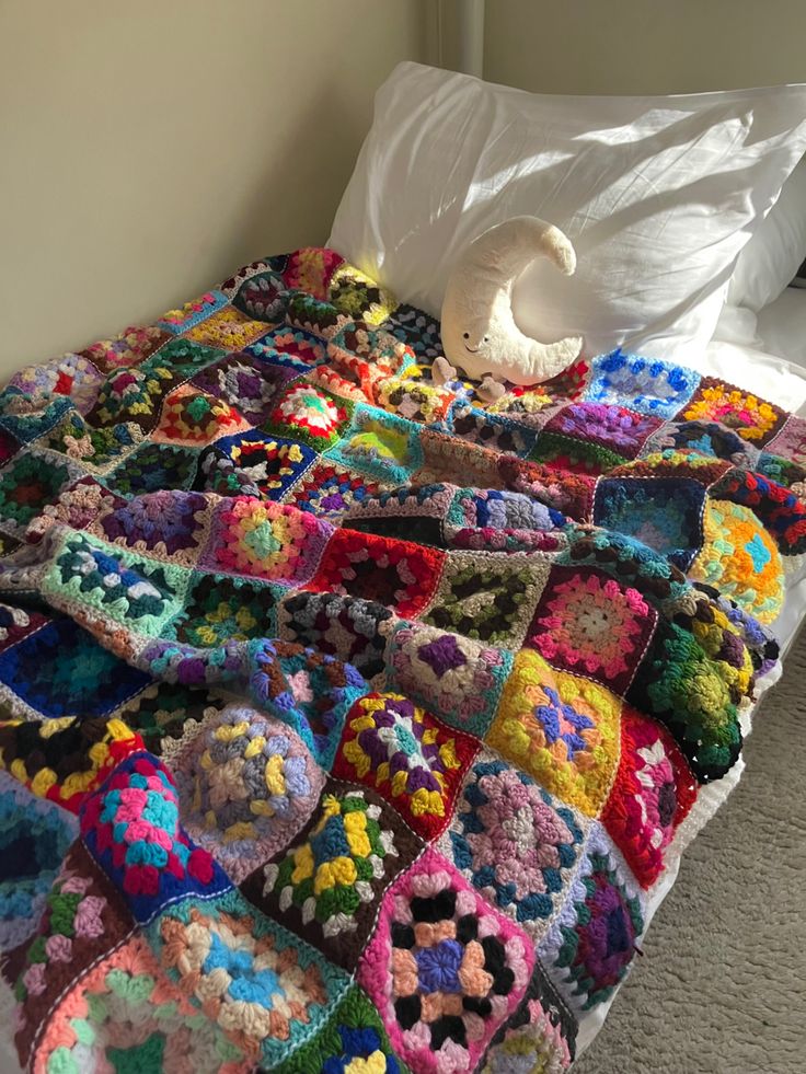 a crocheted granny blanket on a bed with white sheets and pillows in the corner