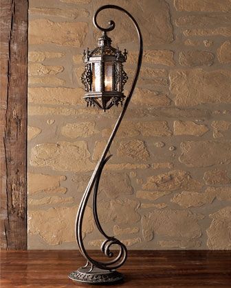 an old fashioned lamp on a table in front of a stone wall and wood floor