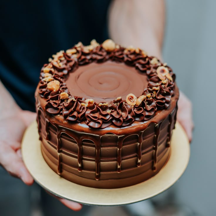 a person holding a chocolate cake with nuts on top and frosting in the middle