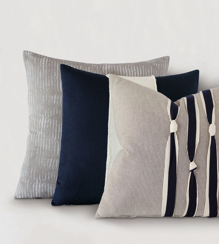 four pillows are lined up against a white wall and one is blue, the other has grey stripes