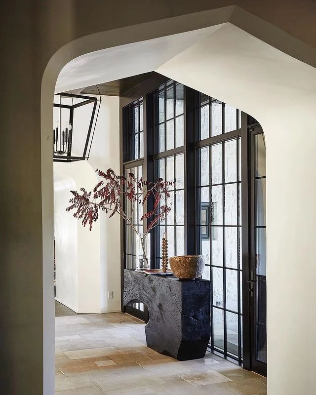 an archway leading into a living room filled with furniture and plants in front of large windows