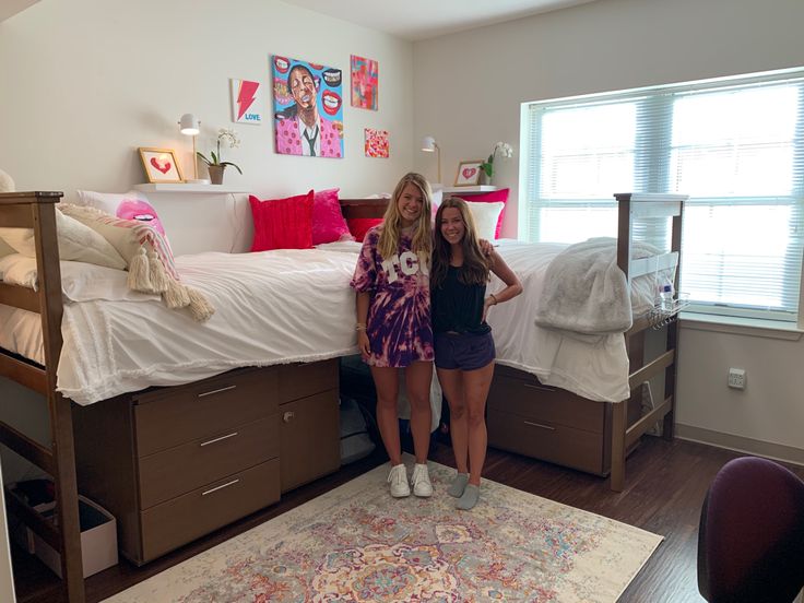 two women standing in front of a bed