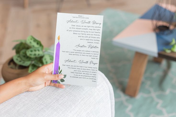 a person holding up a purple candle on top of a white chair with a card in front of it